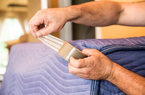 A mover tapes a padded blanket around a piece of furniture before transporting it.  rr